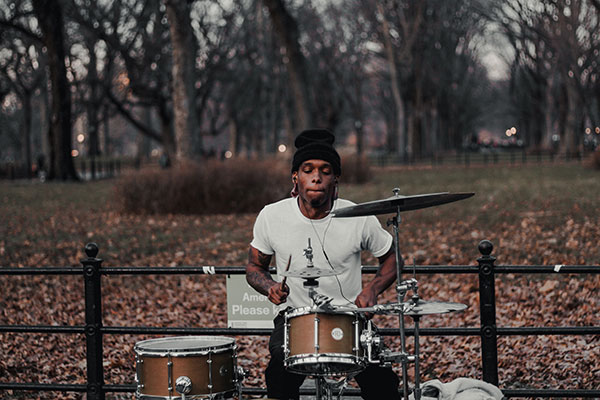 A young man playing a drum kit in a public park