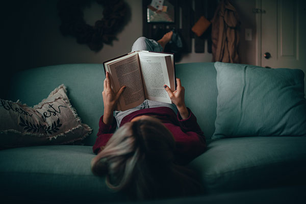 A woman upside down on a couch reading